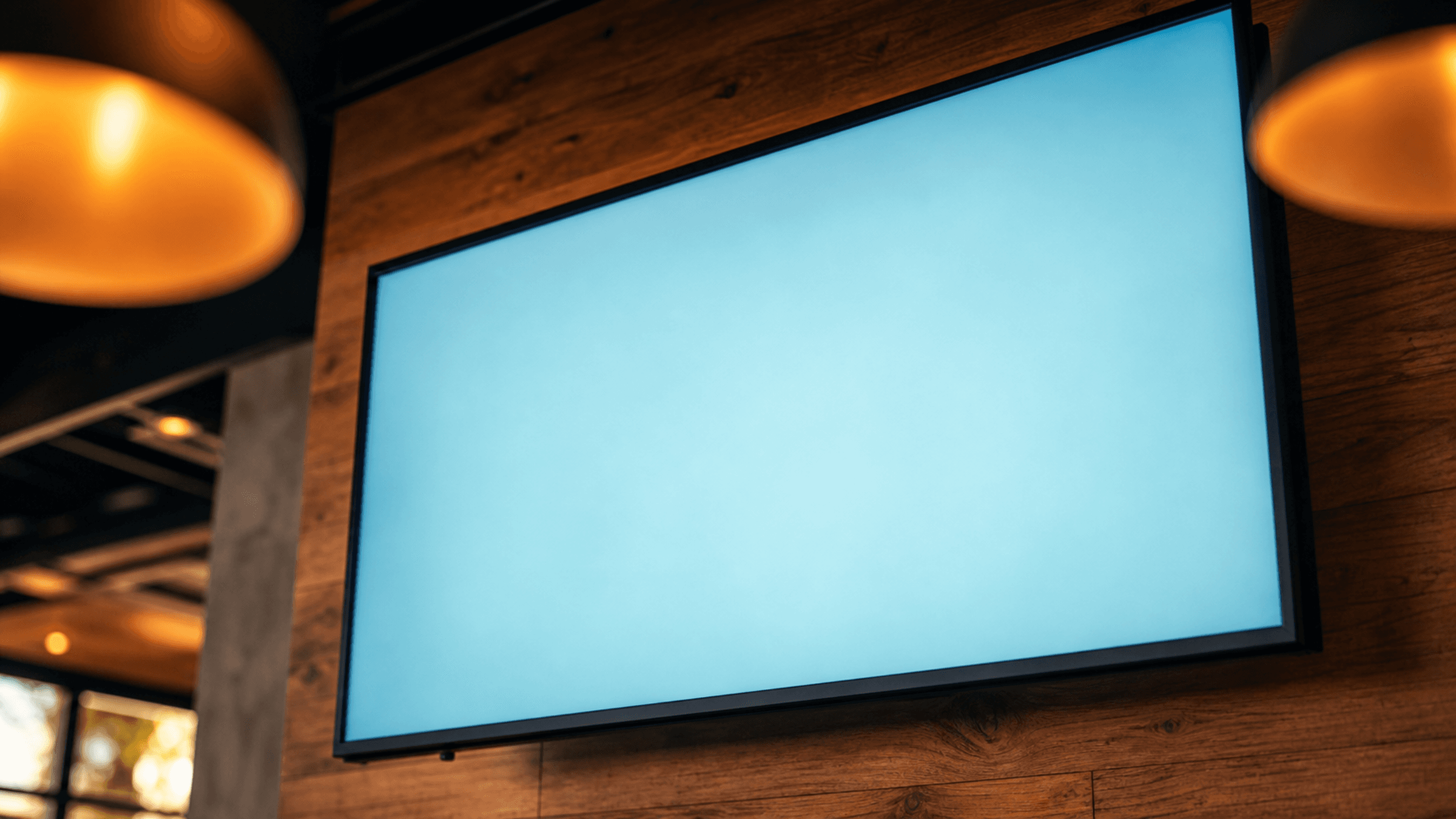 Close-up of a single restaurant TV mounted on a warm wood wall with a softly glowing screen